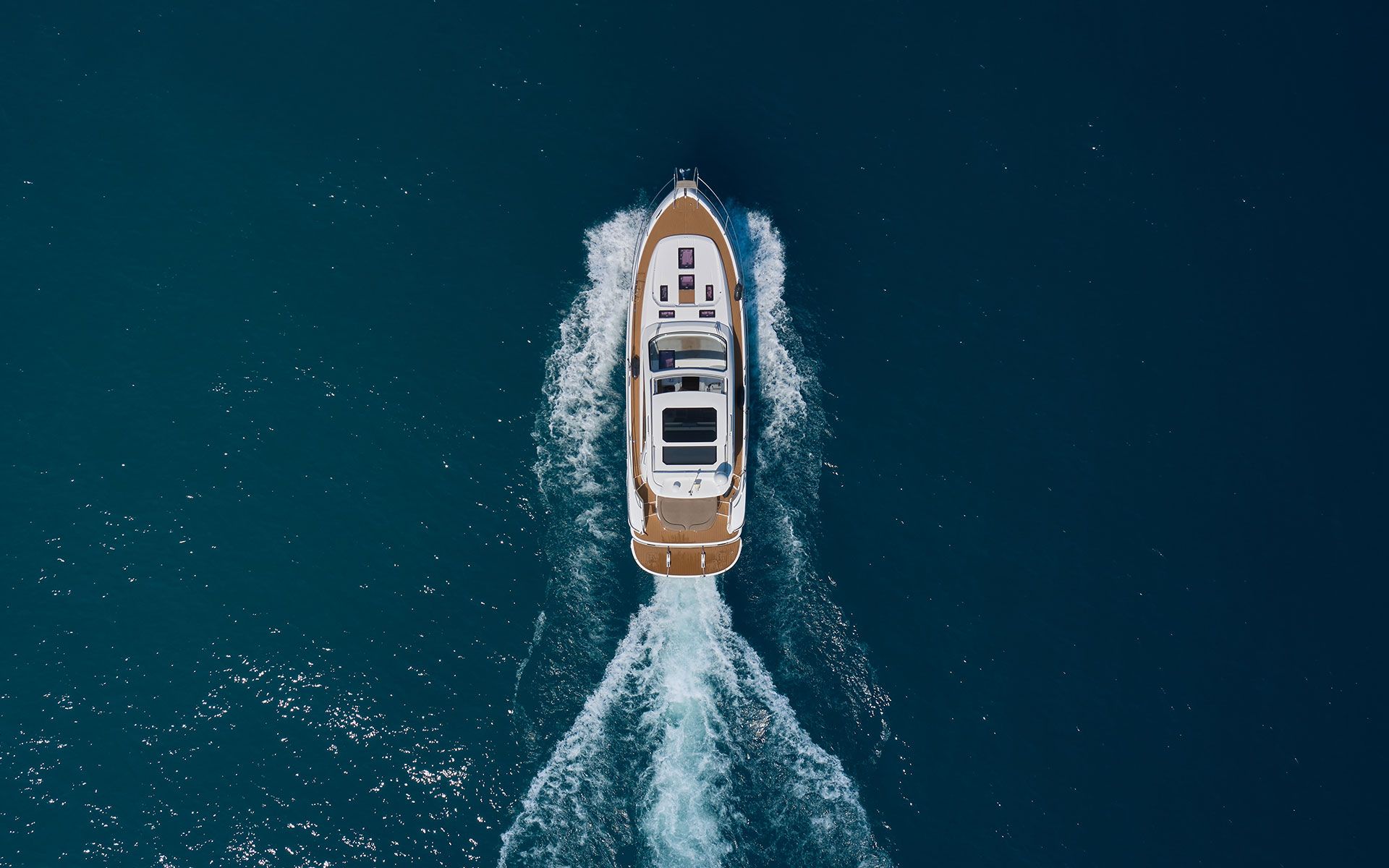 Overhead view of a motor yacht cruising on blue water, creating a white wake.