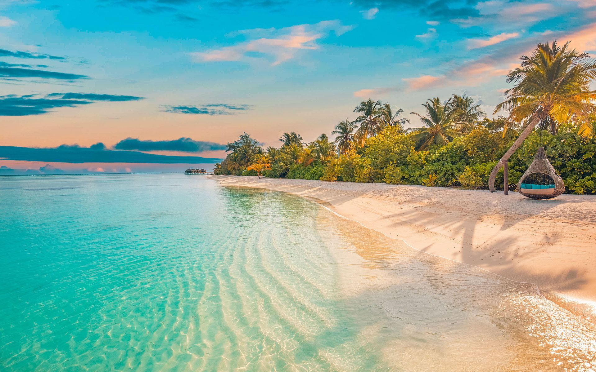 Tropical beach with turquoise water, white sand, palm trees, and a hanging chair.