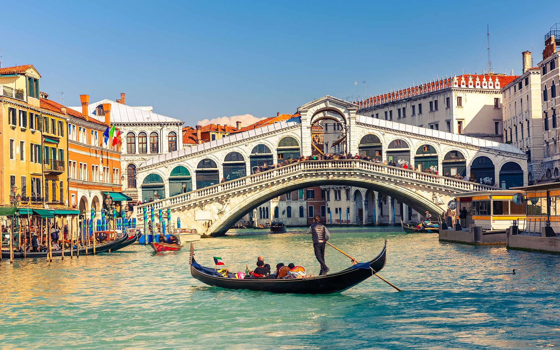 Gondola on canal in Venice, Italy, under the Rialto Bridge. Buildings line the water, sunny day.
