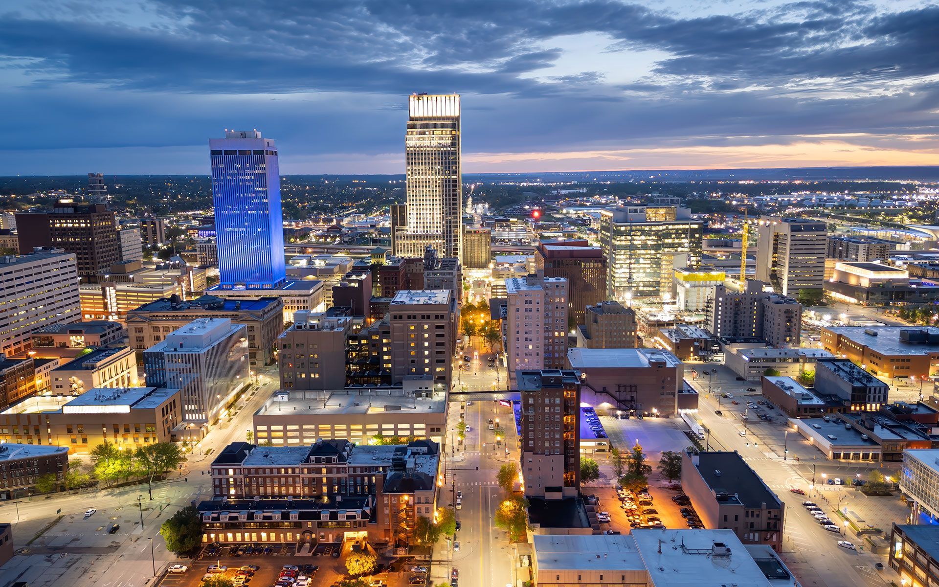 City skyline at dusk; illuminated skyscrapers with lights on, vibrant blue and white.