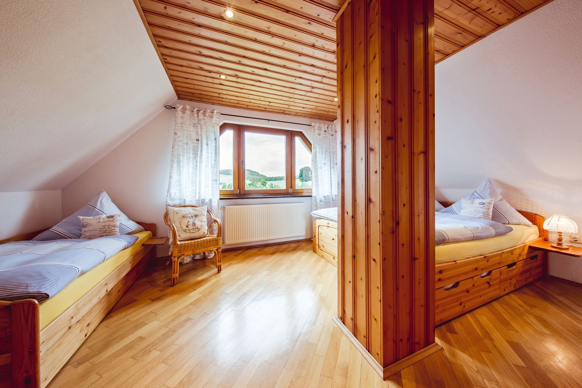 Gemütliches Dachgeschoss-Schlafzimmer mit zwei Einzelbetten, holzgetäfelter Decke und einem Schreibtischbereich am Fenster