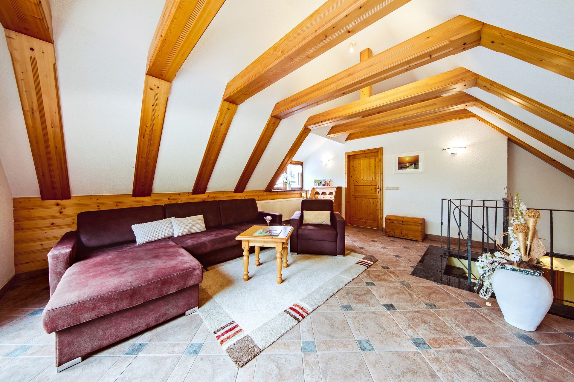 Dachgeschosswohnzimmer mit sichtbaren Holzbalken, Ecksofa, Couchtisch und Fliesenboden