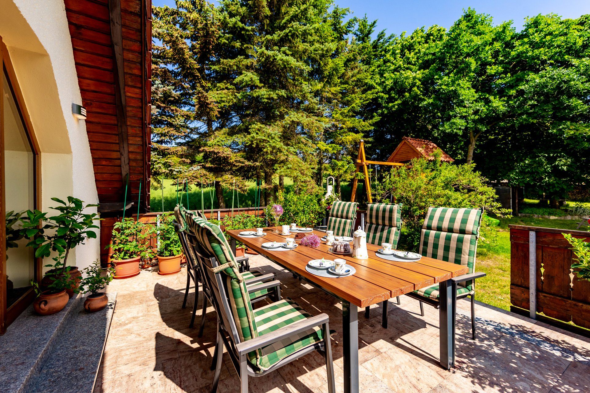 Terrasse mit Holztisch, Stühlen, Topfpflanzen und Gartenblick neben einem Haus