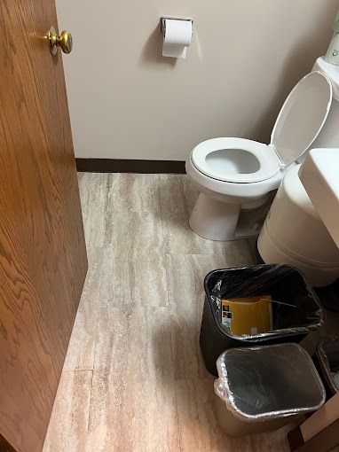 A bathroom with a toilet , sink and trash cans.