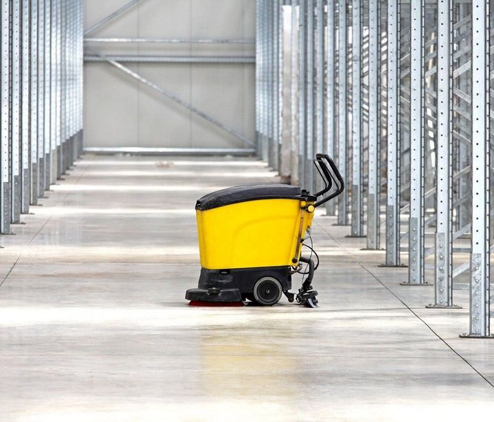 A yellow and black machine is cleaning the floor of a warehouse.