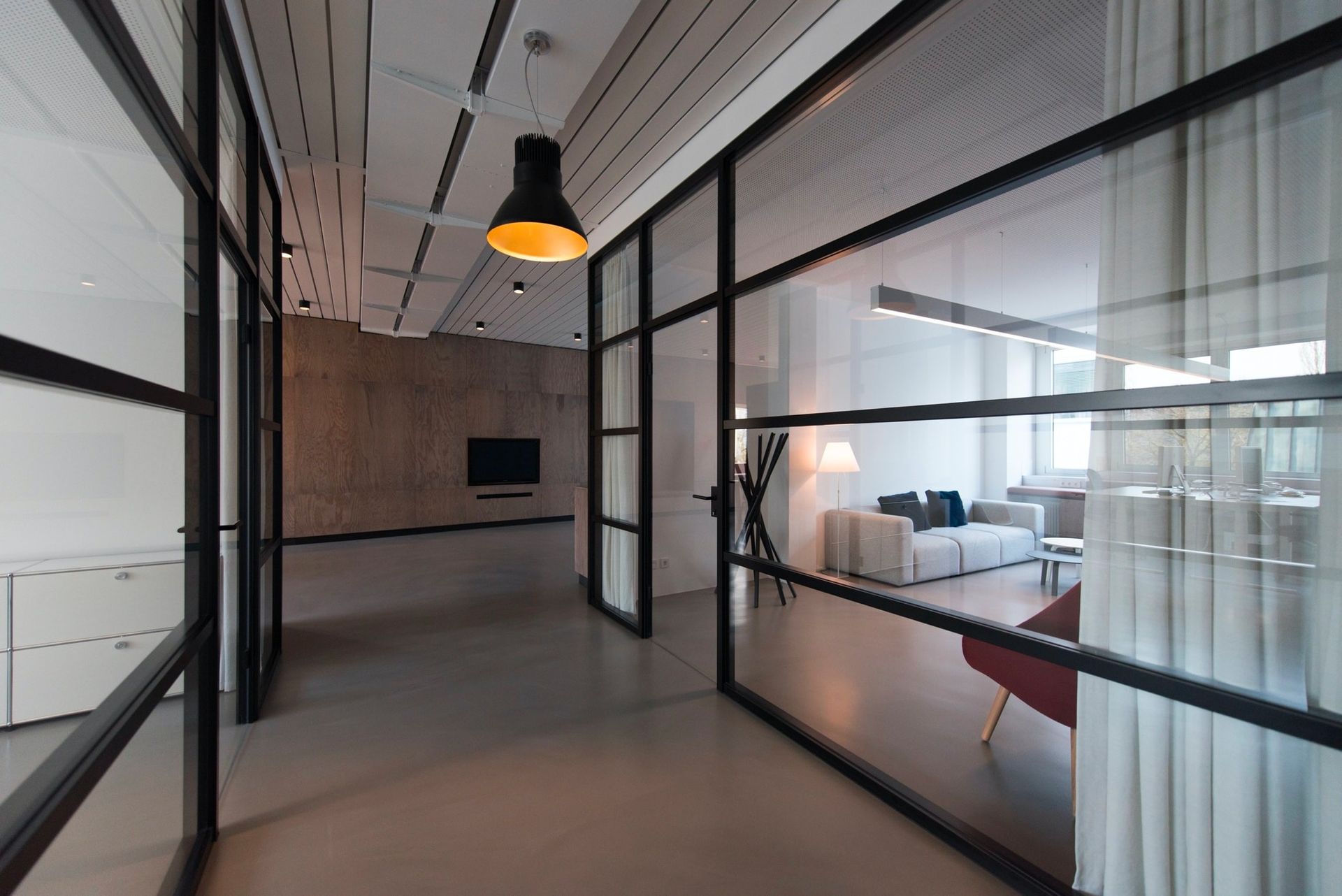 A hallway with a lot of glass walls leading to a living room.