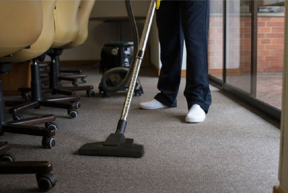 A man is cleaning an office carpet using a vacuum.