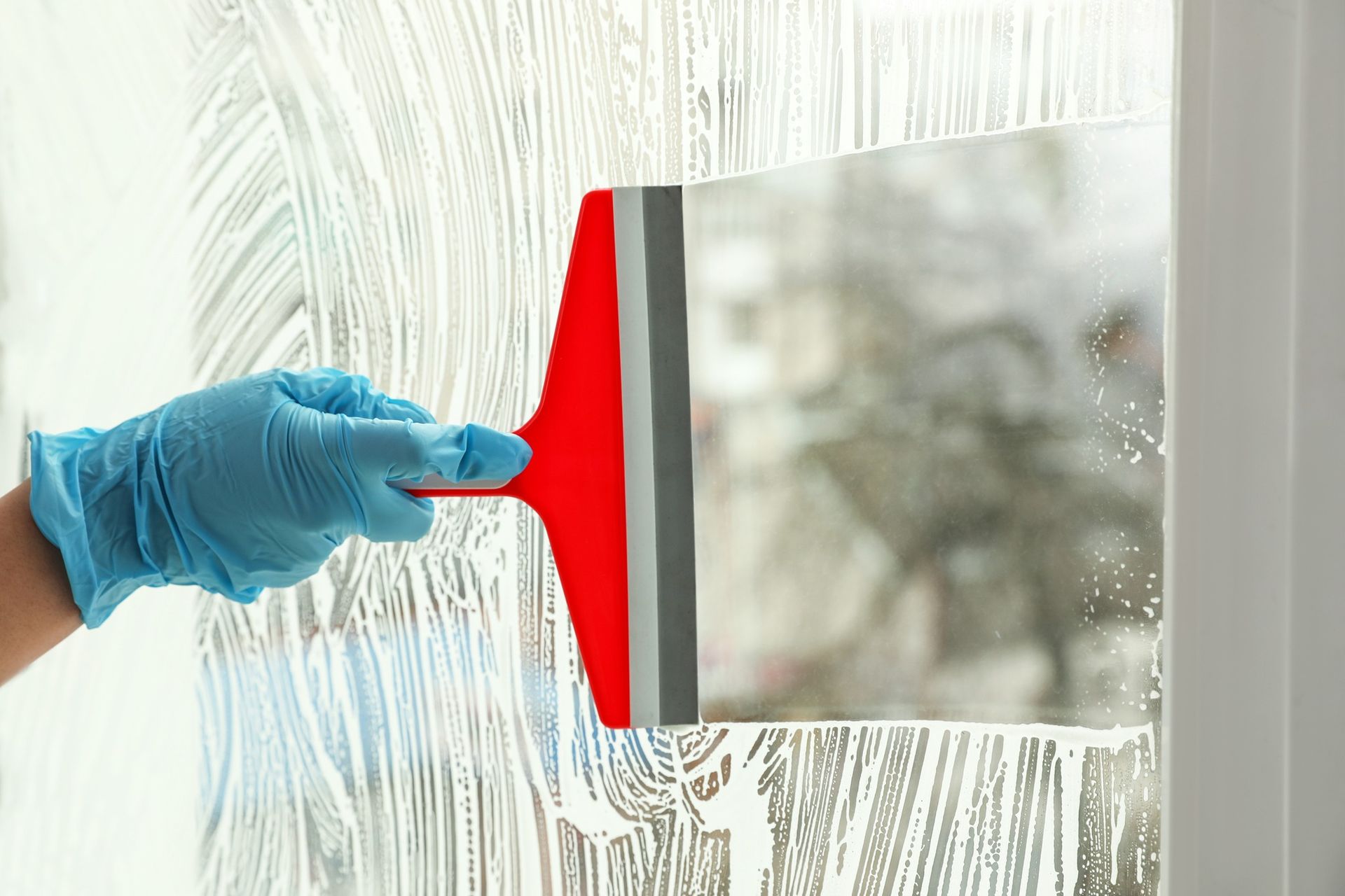 A person wearing a glove is cleaning a window with a squeegee.