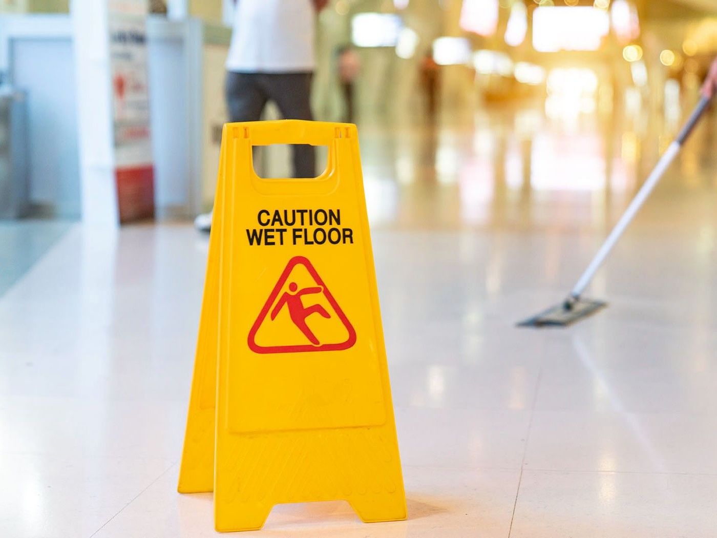 A caution wet floor sign is placed while a cleaner is mopping the floor.