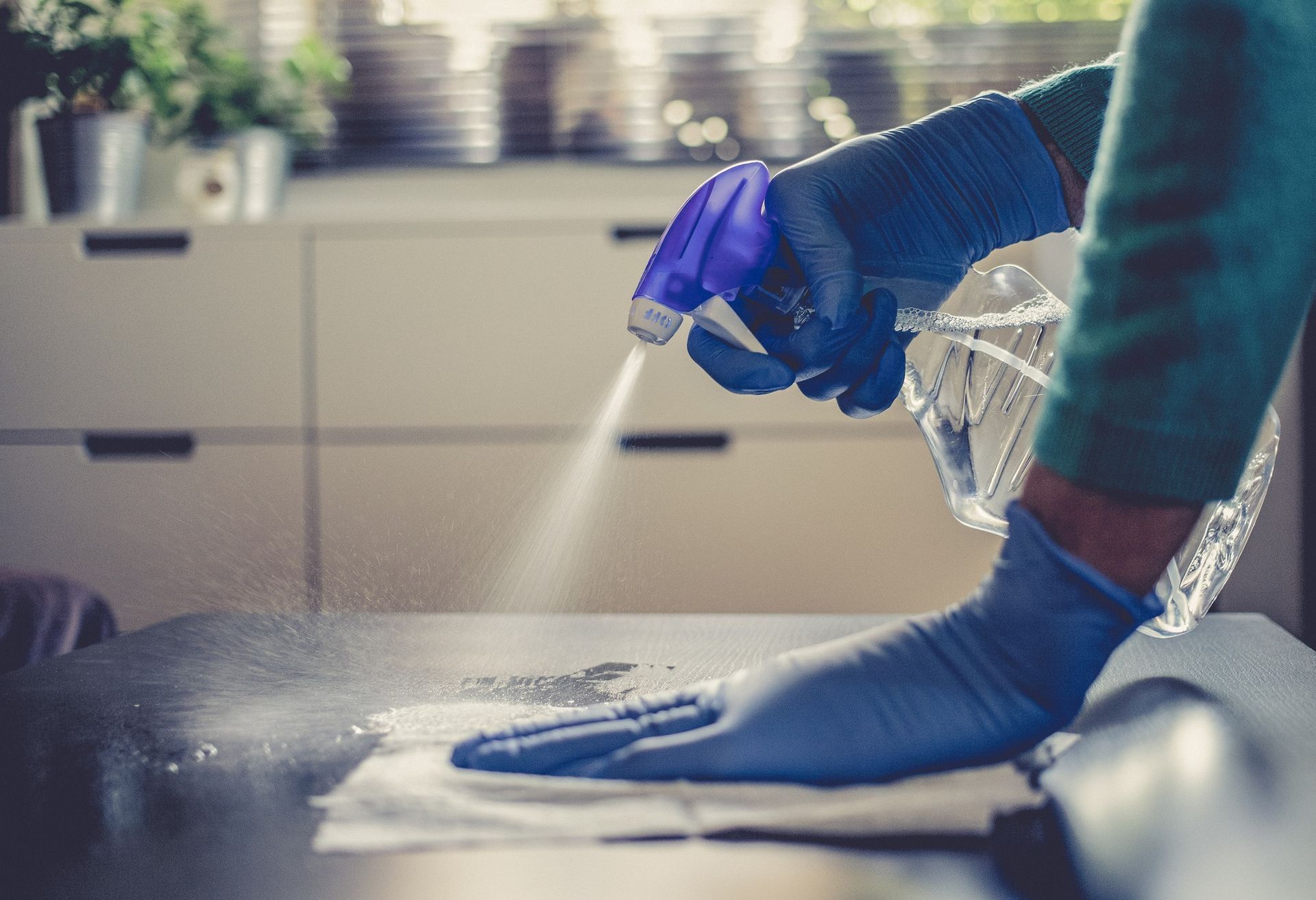 A person wearing blue gloves is cleaning a table with a spray bottle.