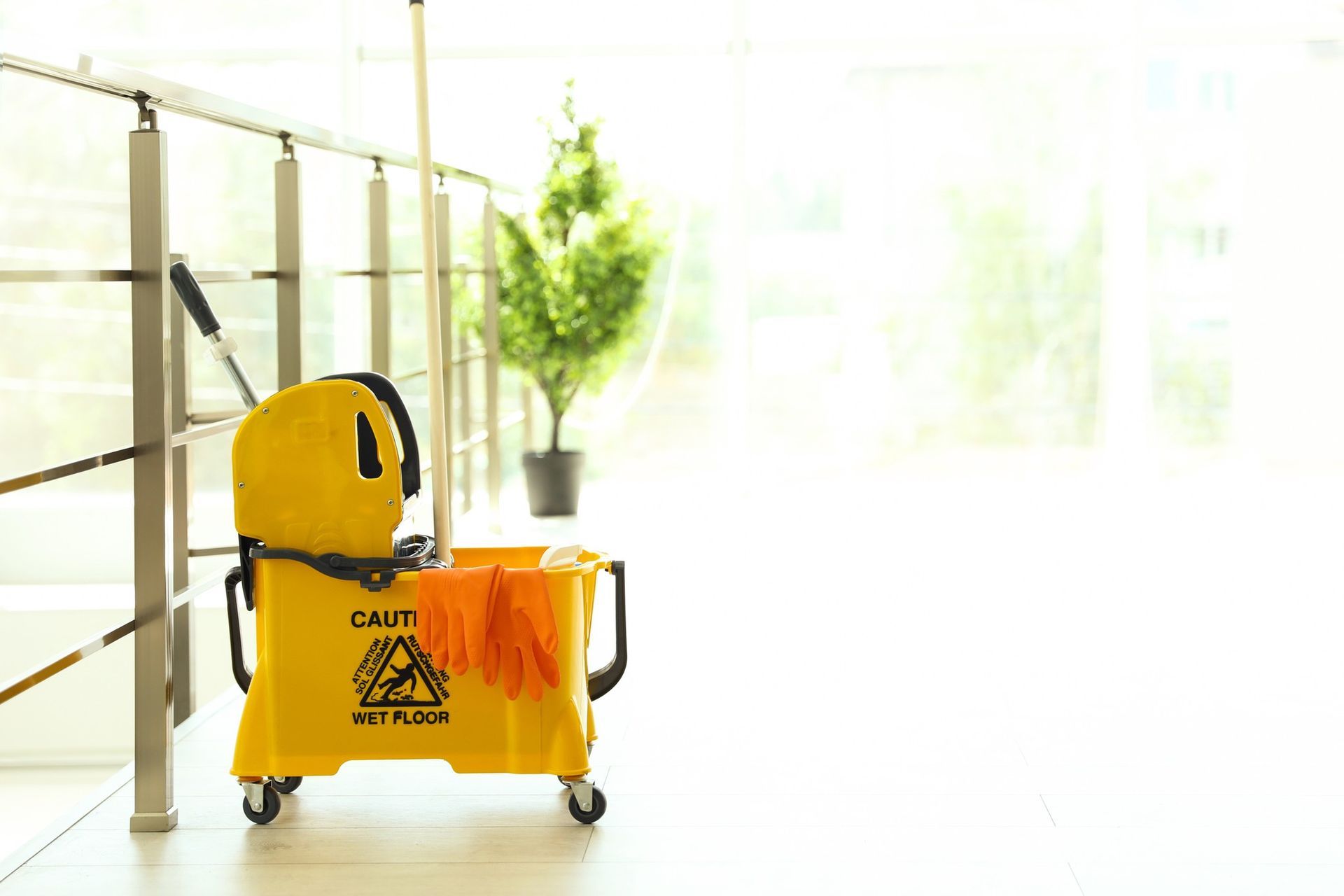 A yellow mop bucket and gloves are sitting next to a railing.