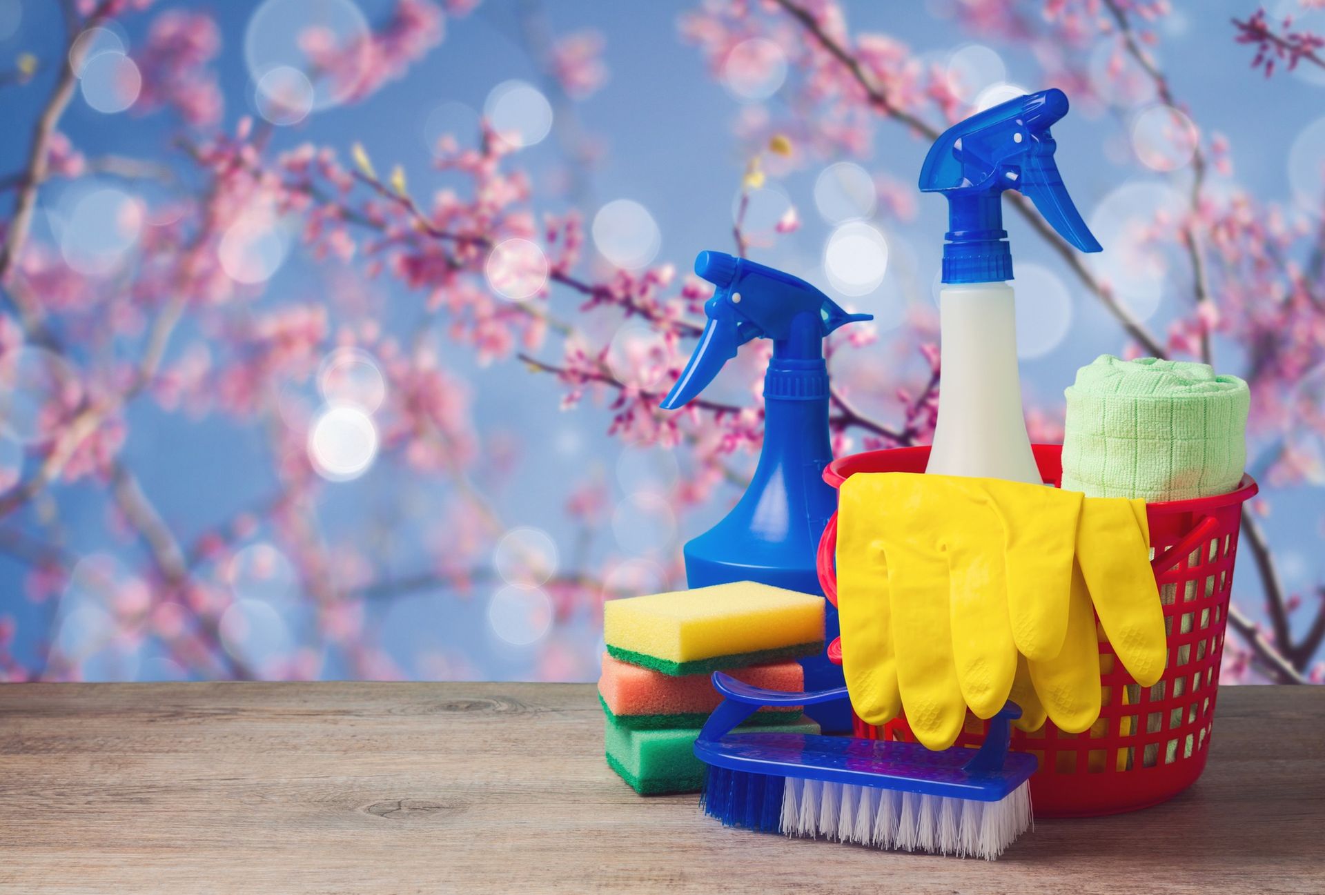 Cleaning supplies are sitting on a wooden table in front of a cherry blossom tree.