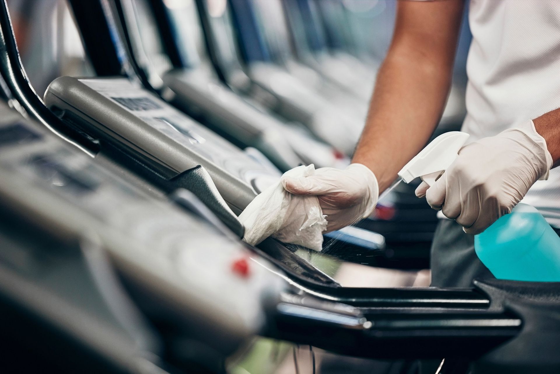 A man is cleaning a treadmill in a gym.