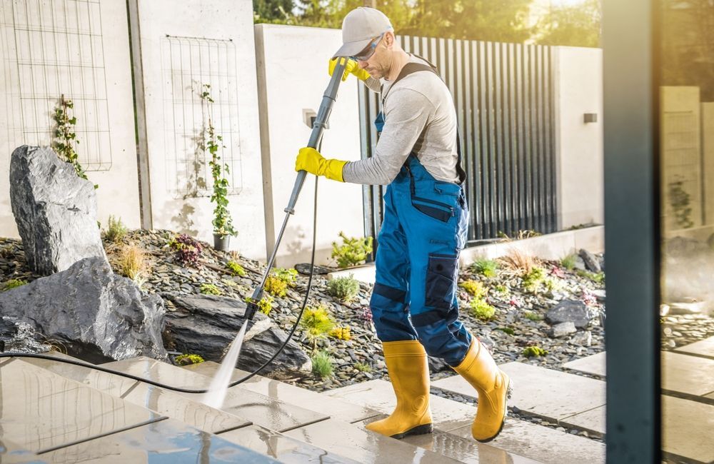 A man is using a high pressure washer to clean a sidewalk.