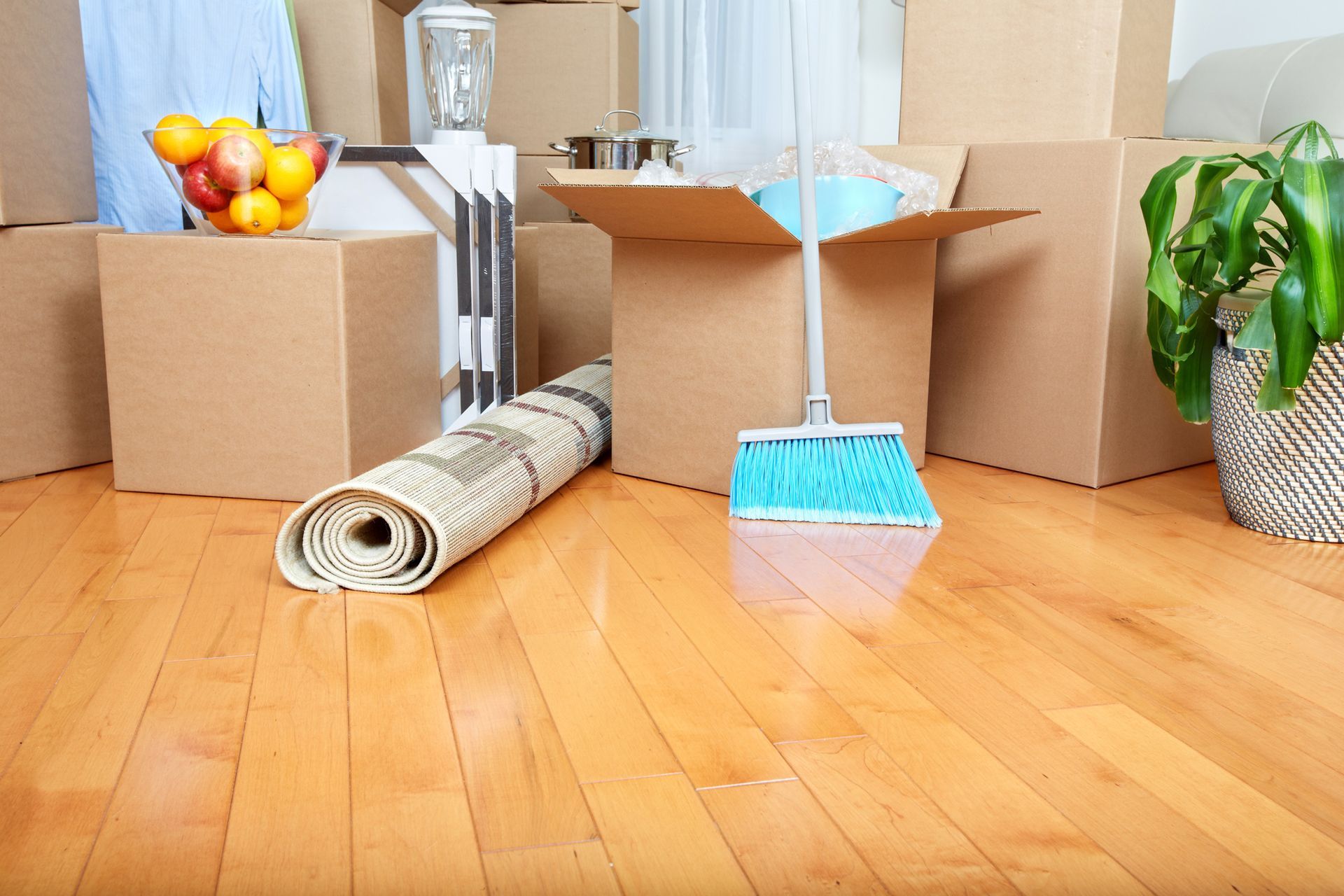 A broom is sitting on a wooden floor surrounded by cardboard boxes.