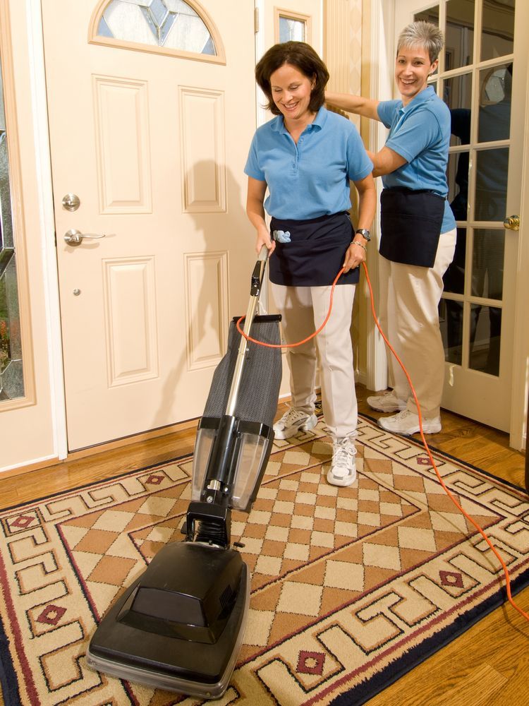 Two women are cleaning a rug with a vacuum cleaner.