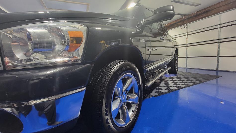 A black truck is parked in a garage with a blue floor.