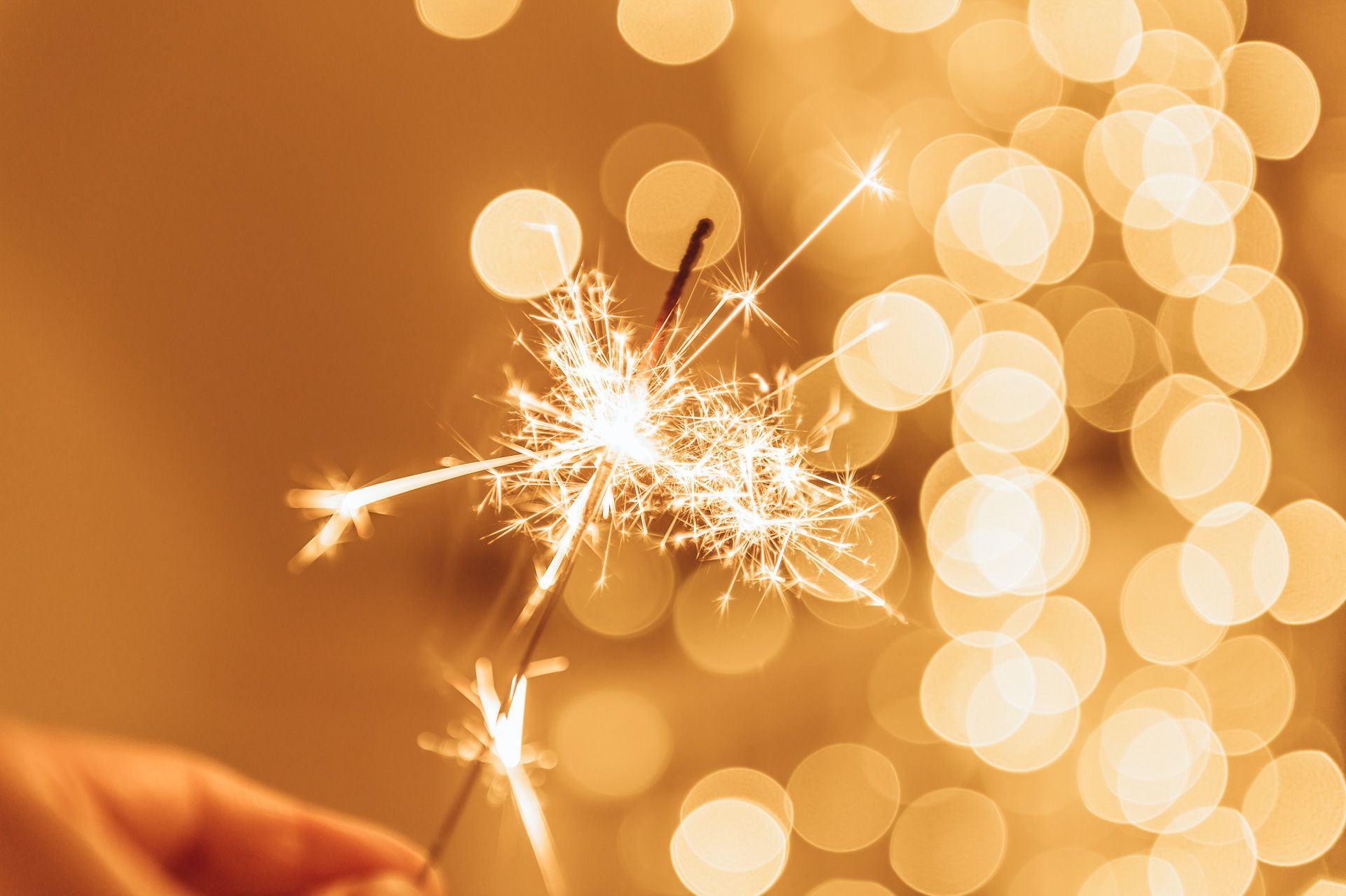A person is holding a sparkler in their hand in front of a christmas tree.