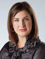 A woman is wearing a black ruffled blouse and earrings.