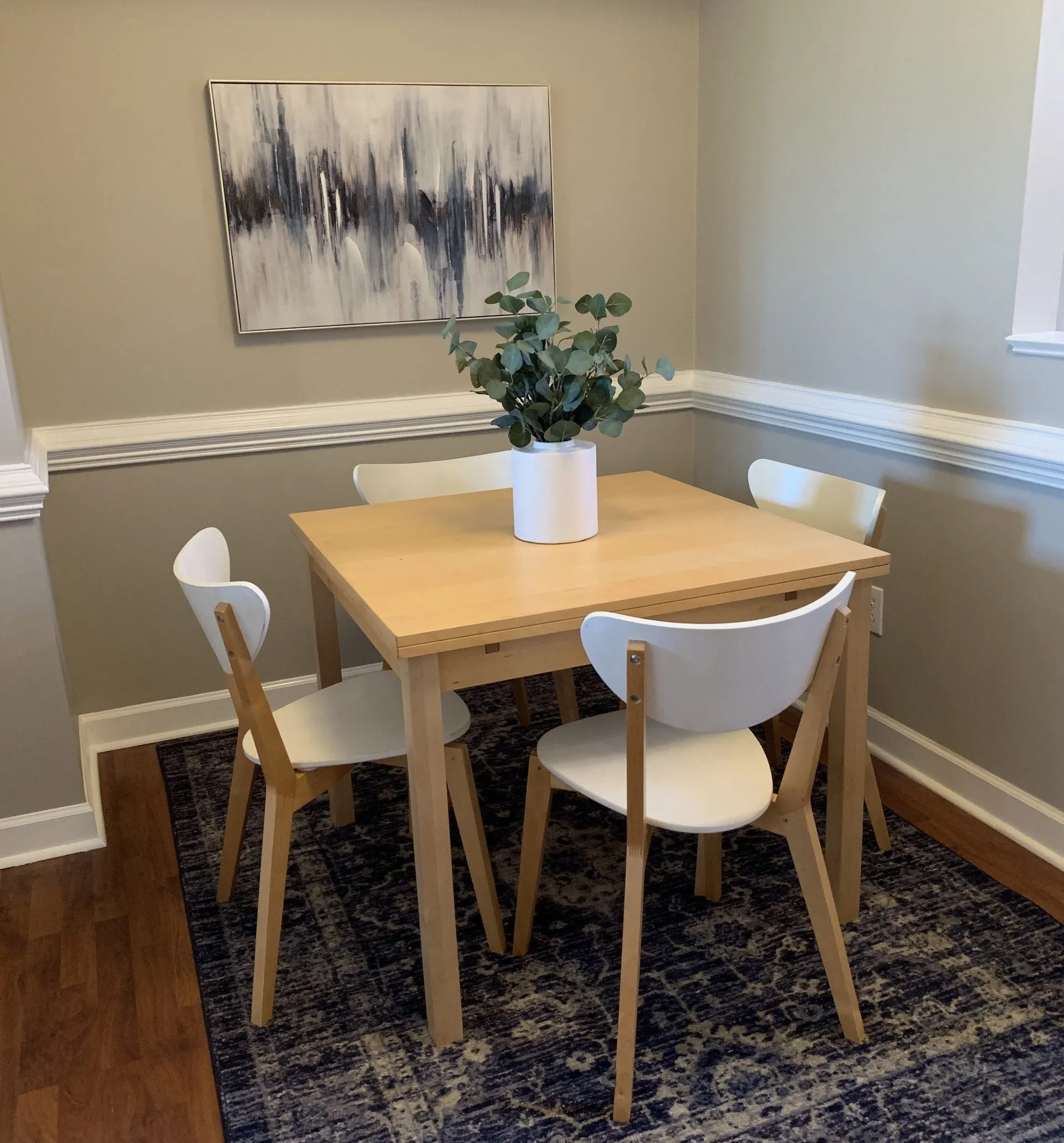 A dining room with a table and chairs and a painting on the wall.