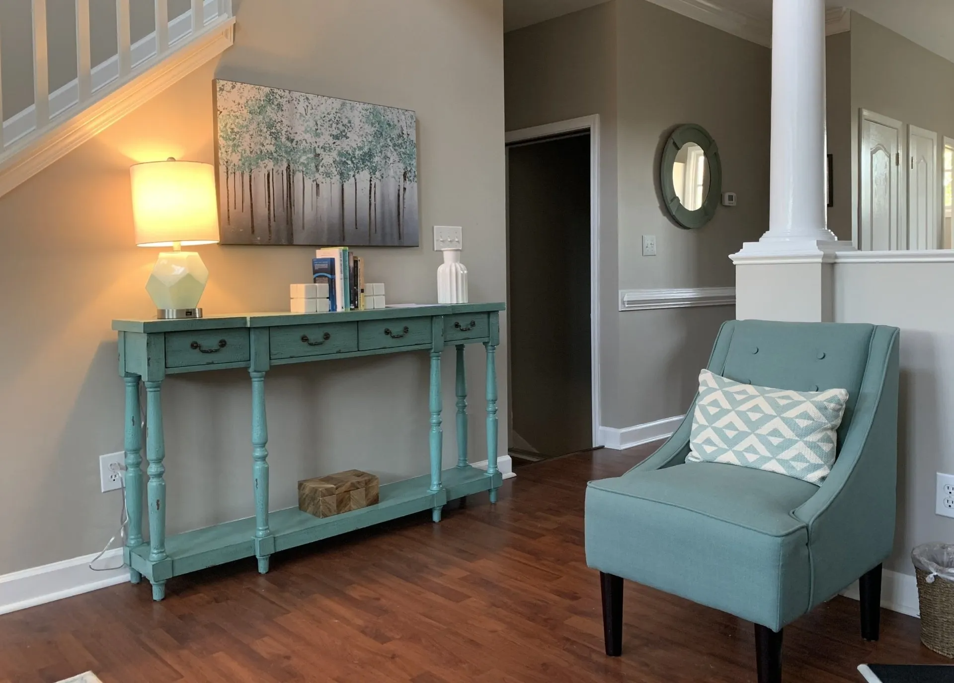 A living room with a table , chair , lamp and stairs.