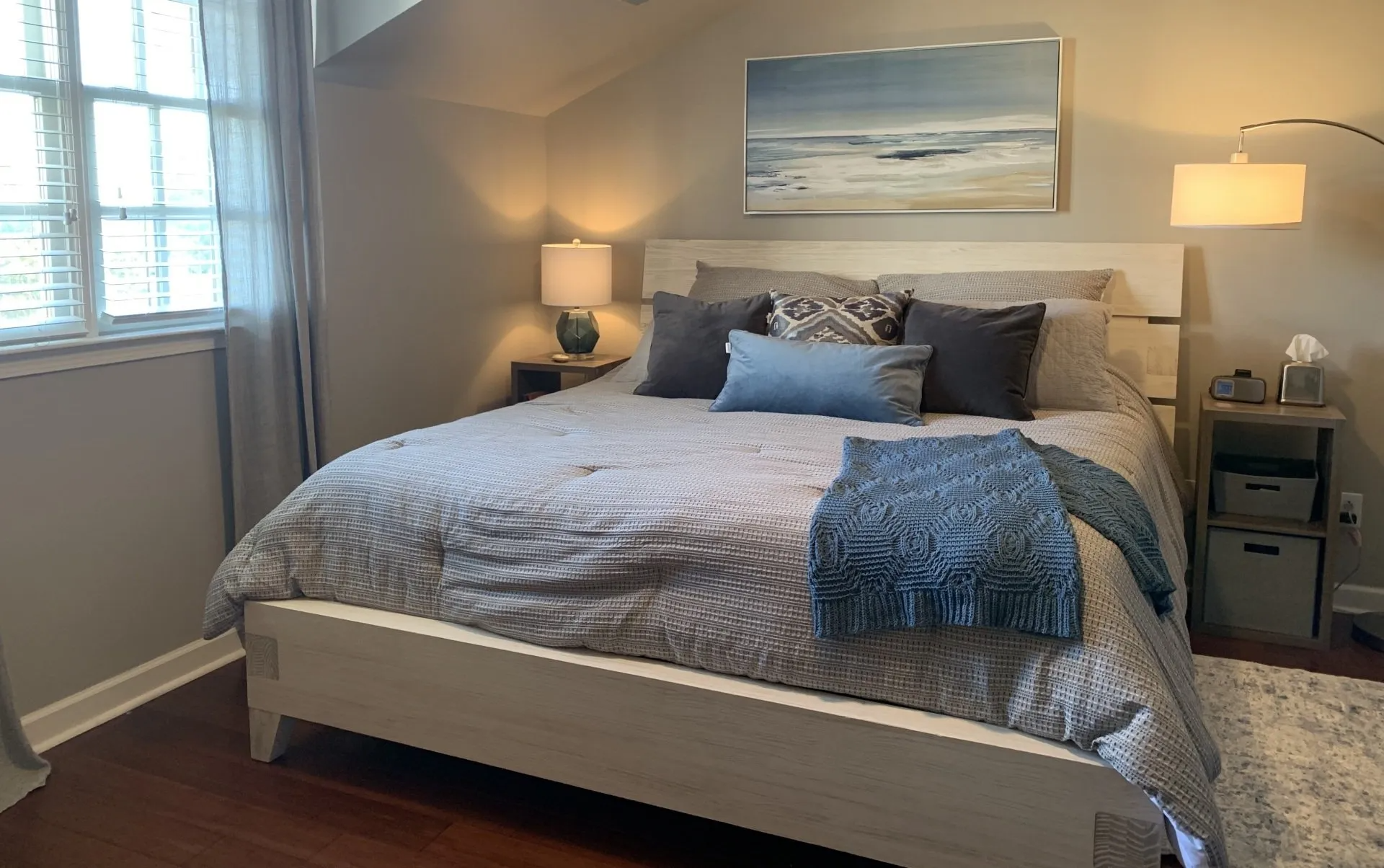 A bedroom with a bed , lamps , and a painting on the wall.
