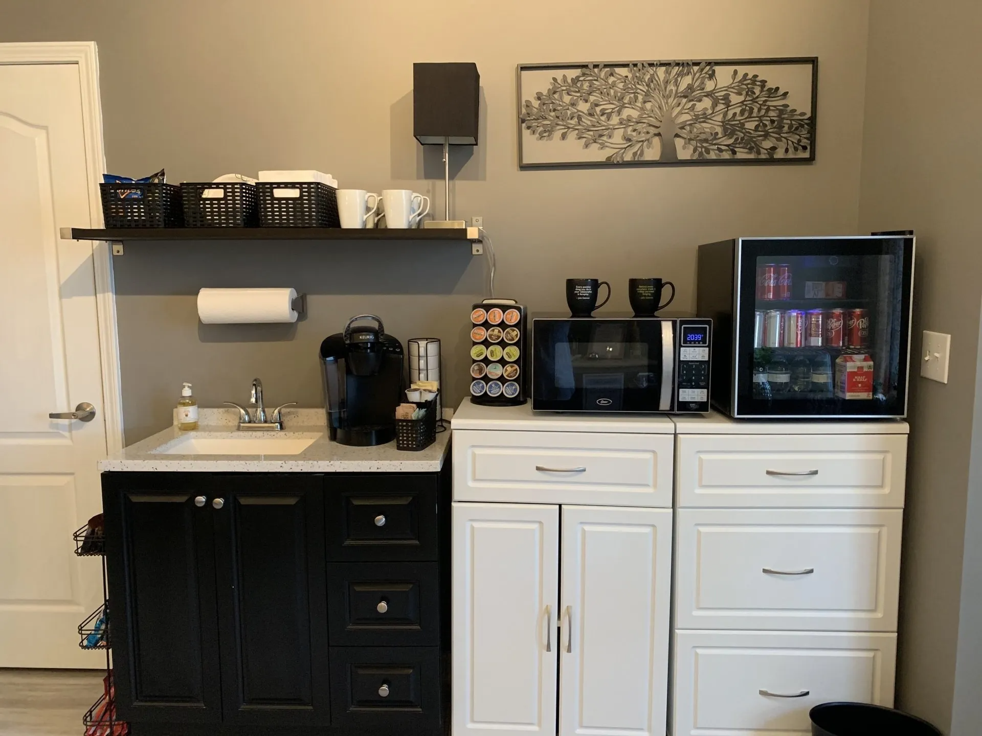 A kitchen with black and white cabinets , a sink , a microwave , and a refrigerator.
