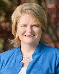 A woman is wearing a blue jacket and smiling for the camera.
