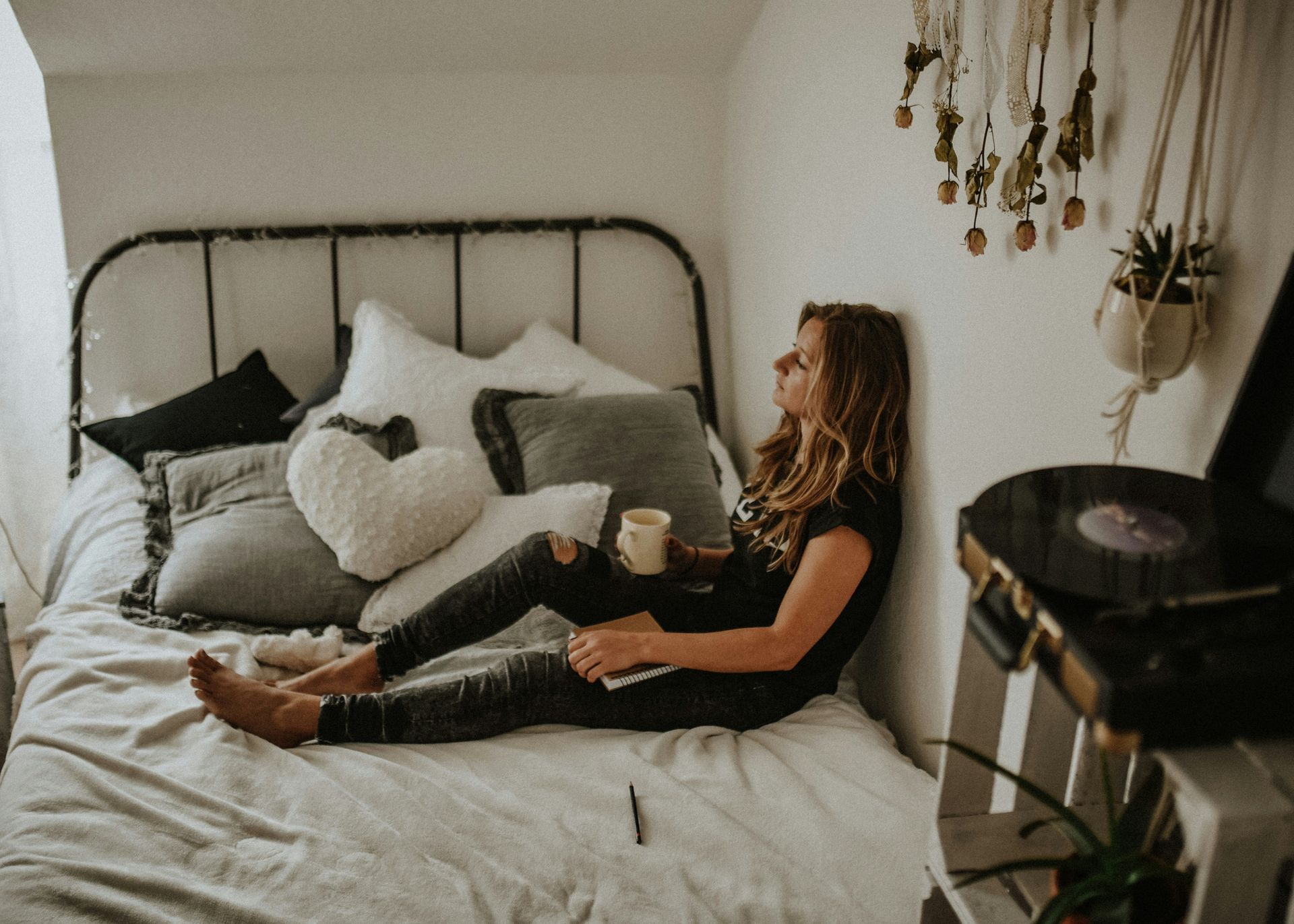 A woman is sitting on a bed with a cup of coffee.