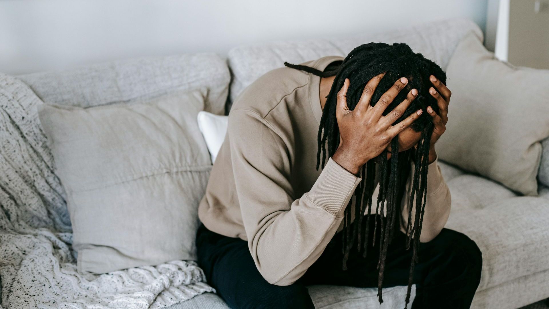 A man is sitting on a couch with his head in his hands.