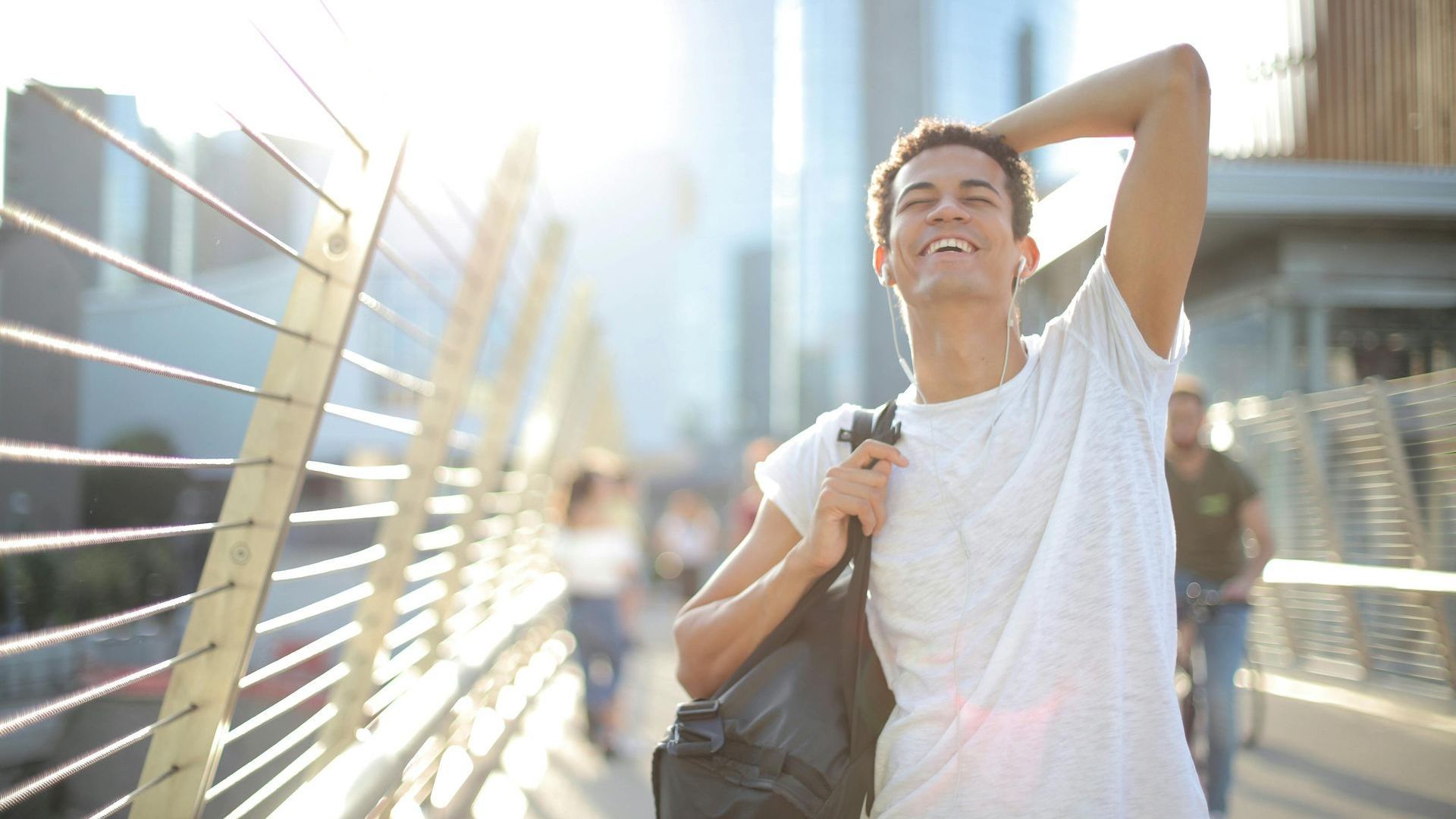 A young man is walking across a bridge with a backpack.