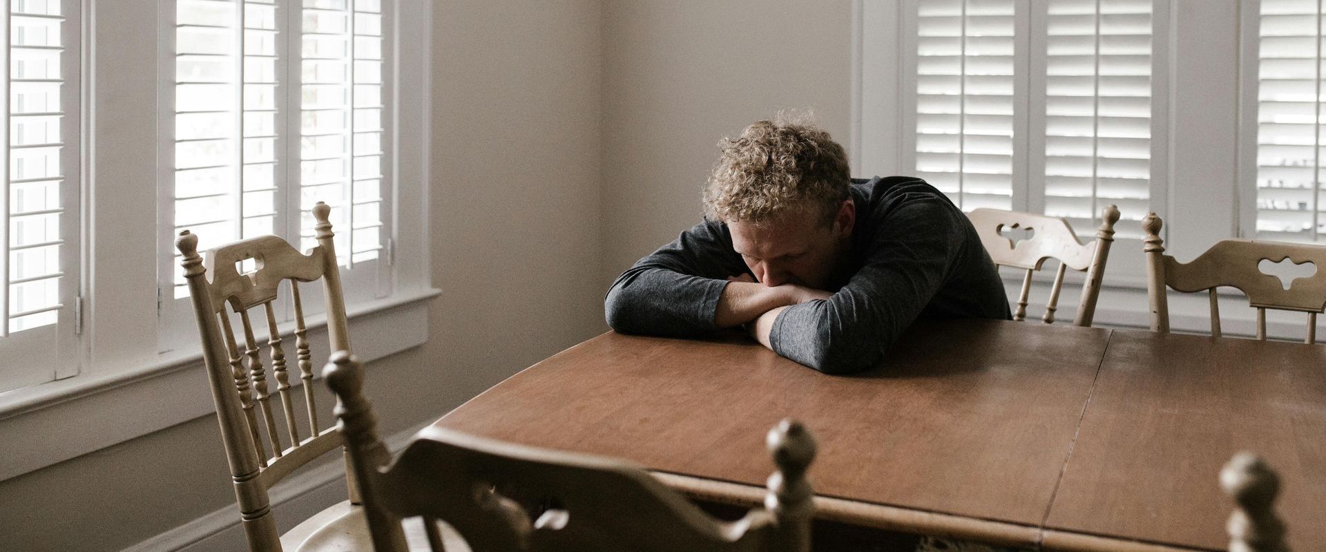 A man is sitting at a table with his head on his hands.