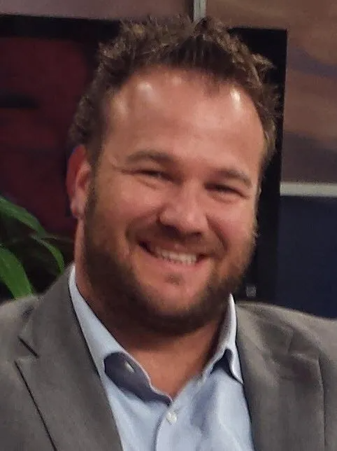 A man in a suit and blue shirt smiles for the camera