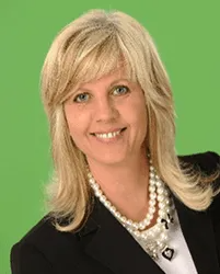 A woman wearing a pearl necklace and a black jacket is smiling.