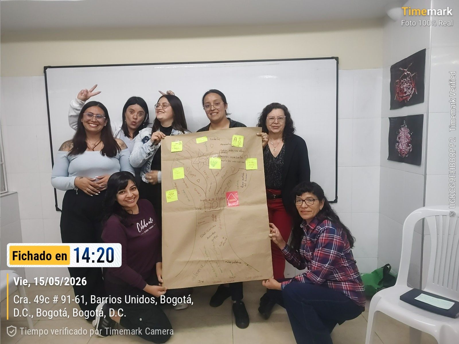 Grupo de personas posando con un gran póster de papel cubierto de notas adhesivas en un aula.