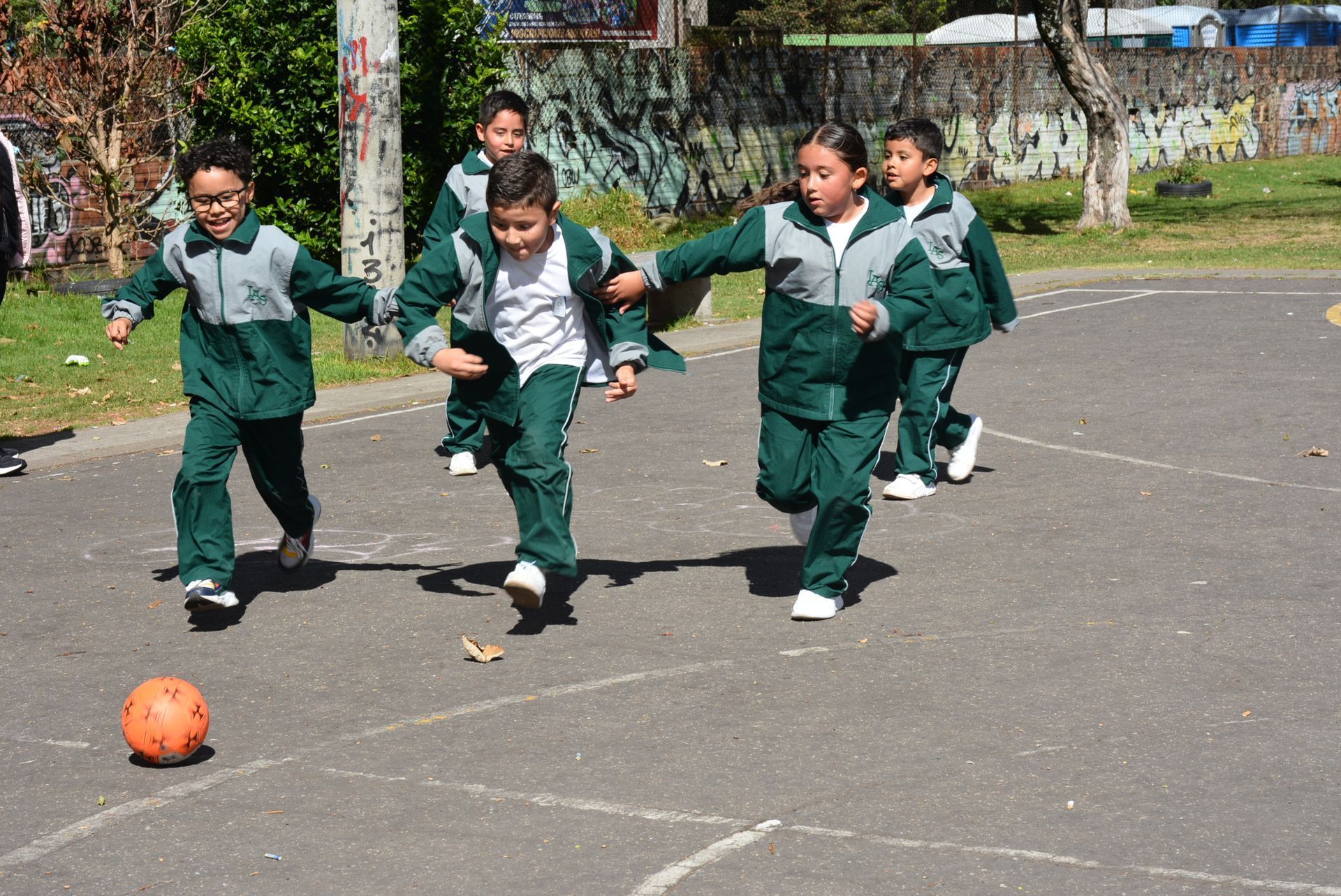 Niños con chándales verdes jugando al fútbol en el patio de una escuela.