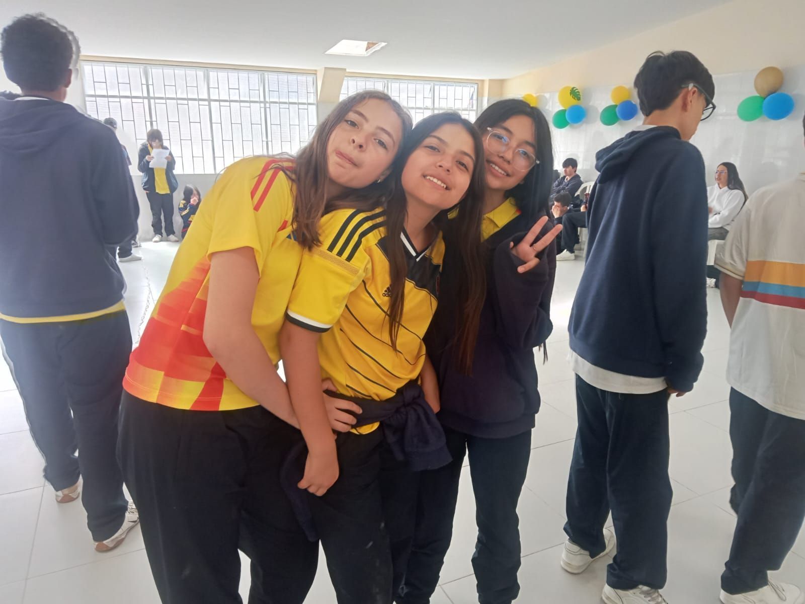 Tres amigos posando juntos en una fiesta en un espacio cerrado, sonriendo y vistiendo camisetas amarillas y negras.