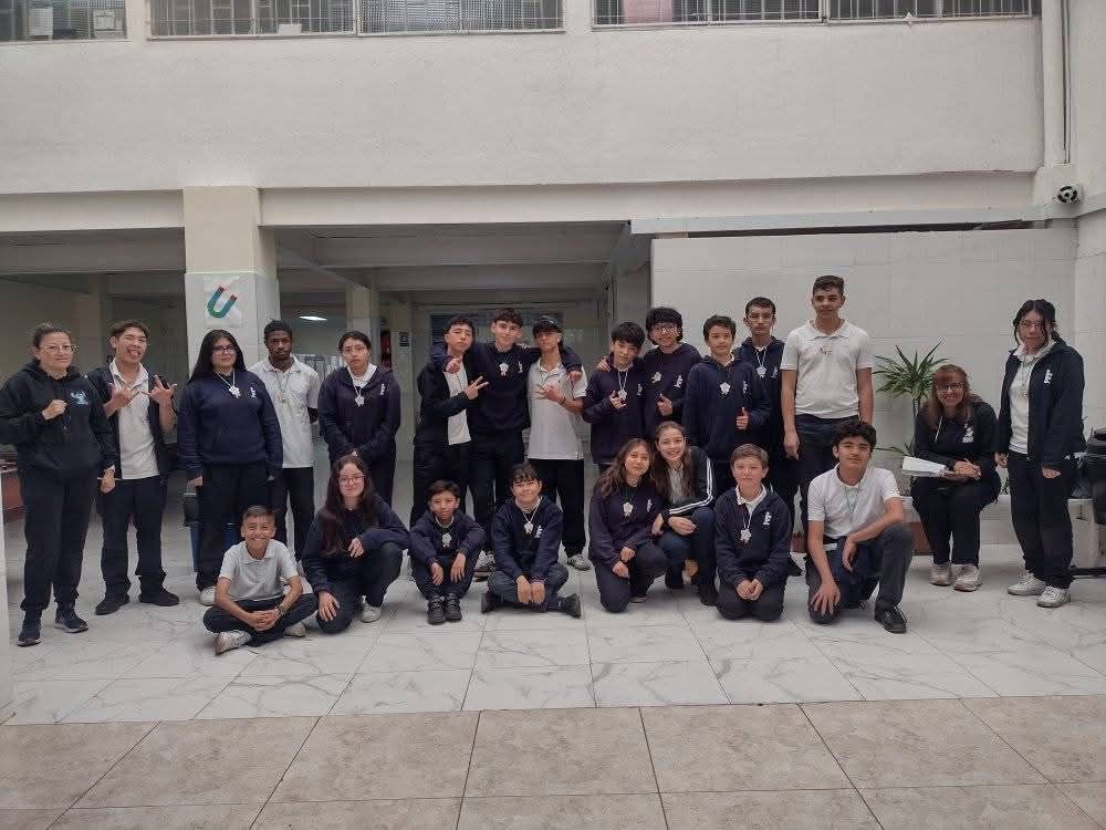 Grupo de personas posando al aire libre frente a un edificio, algunas de pie y otras agachadas.