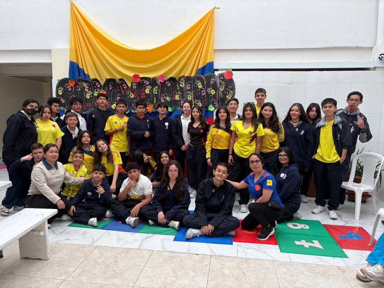Foto grupal de personas posando en interiores frente a un telón de fondo amarillo y rojo.