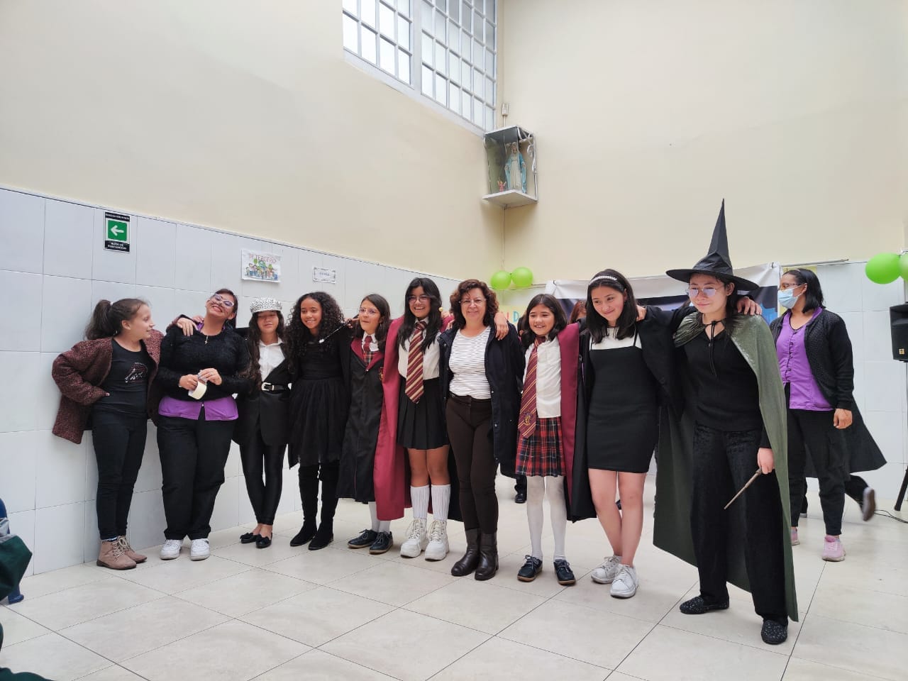 Grupo de personas posando en el interior, disfrazadas, con sombrero de bruja y atuendos negros, en una habitación luminosa.