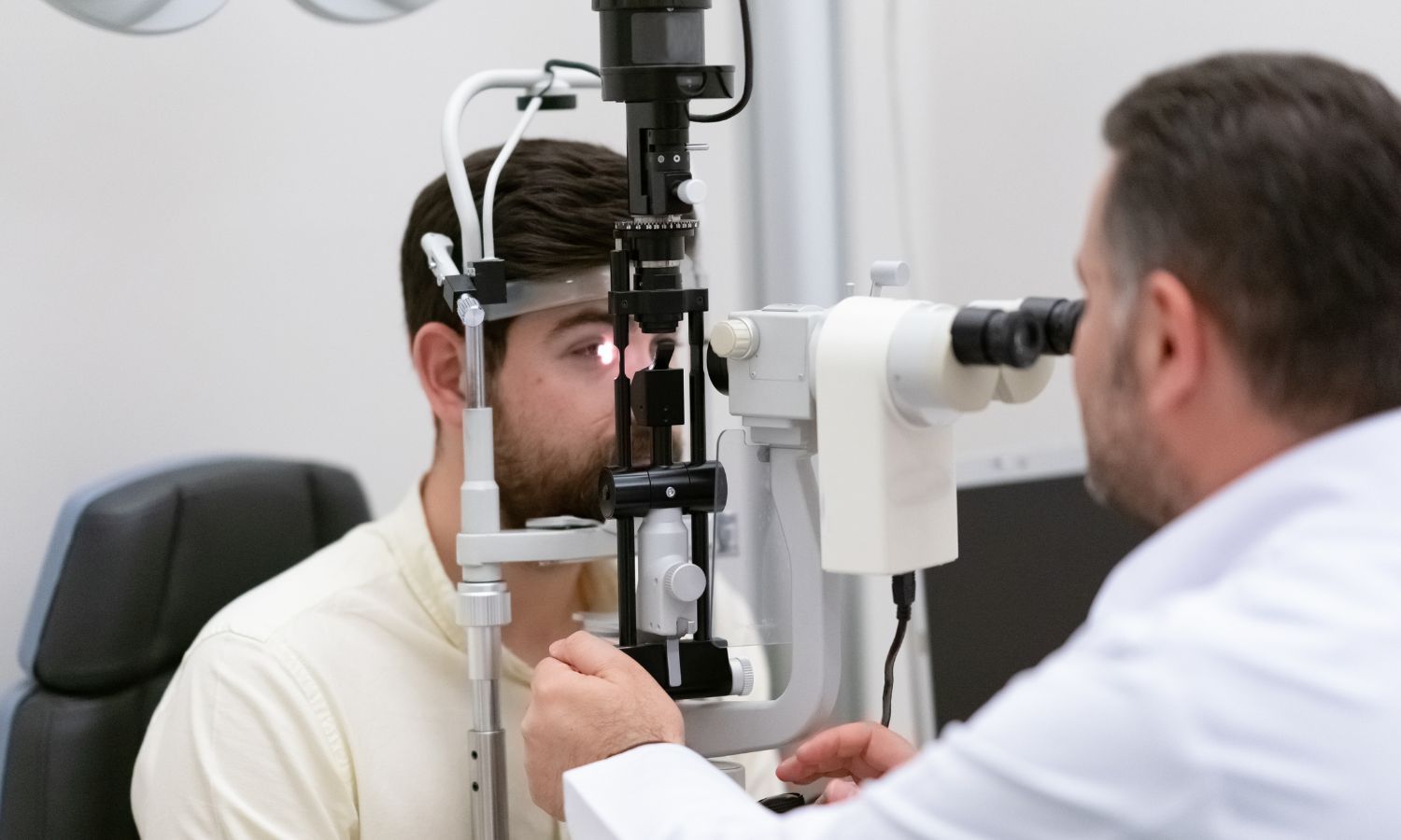 Man undergoing an eye exam with a doctor using a slit lamp to examine his eye in an office setting.