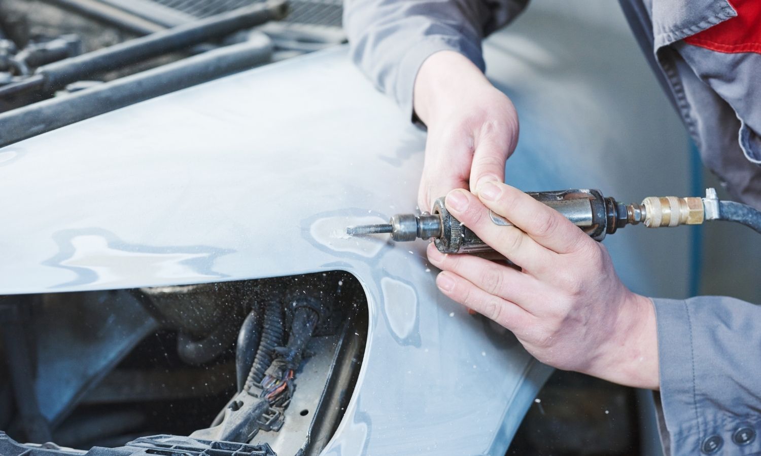 Mechanic using a grinder on a car fender in a repair shop.