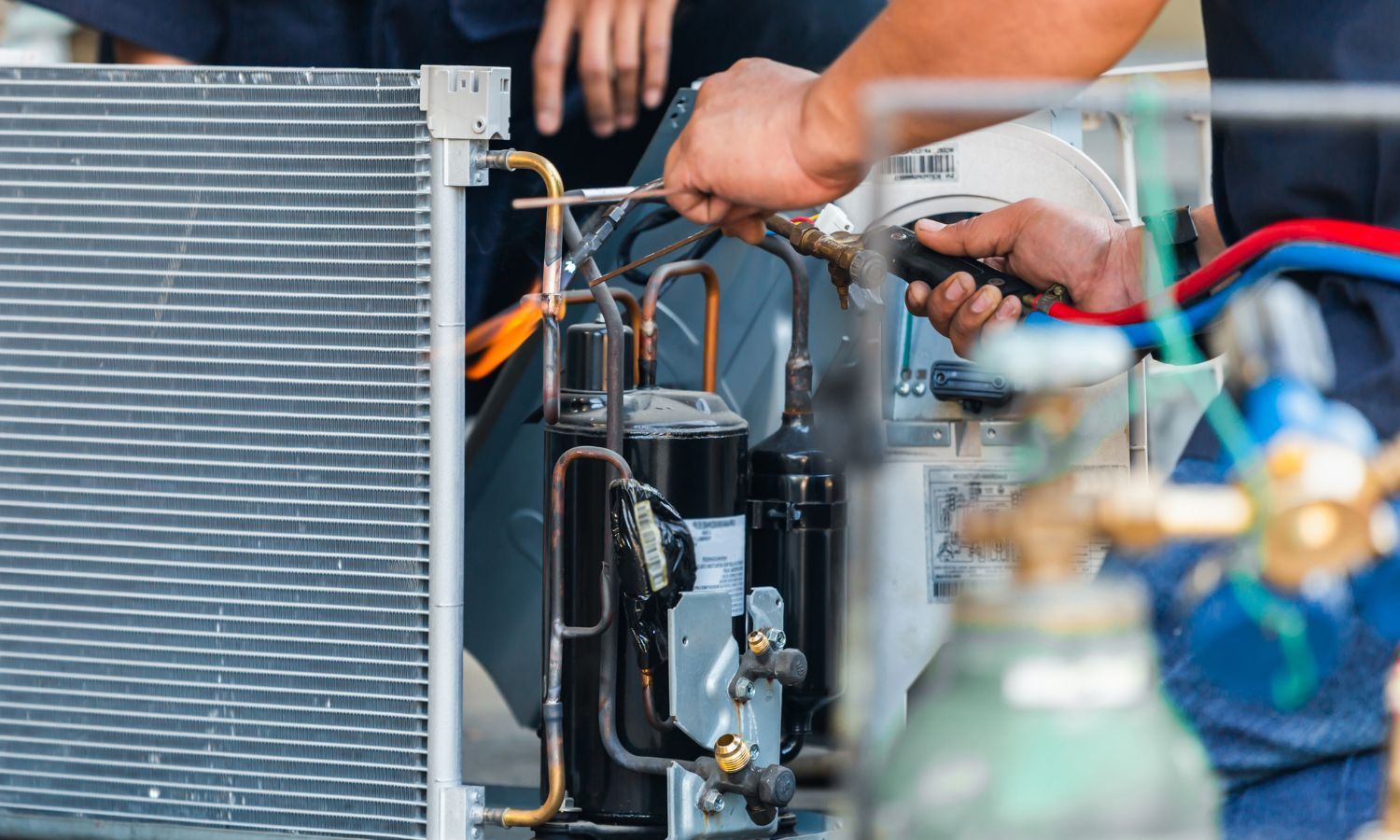 Hands working on AC unit; outdoor setting. Repairing refrigerant lines with tools.