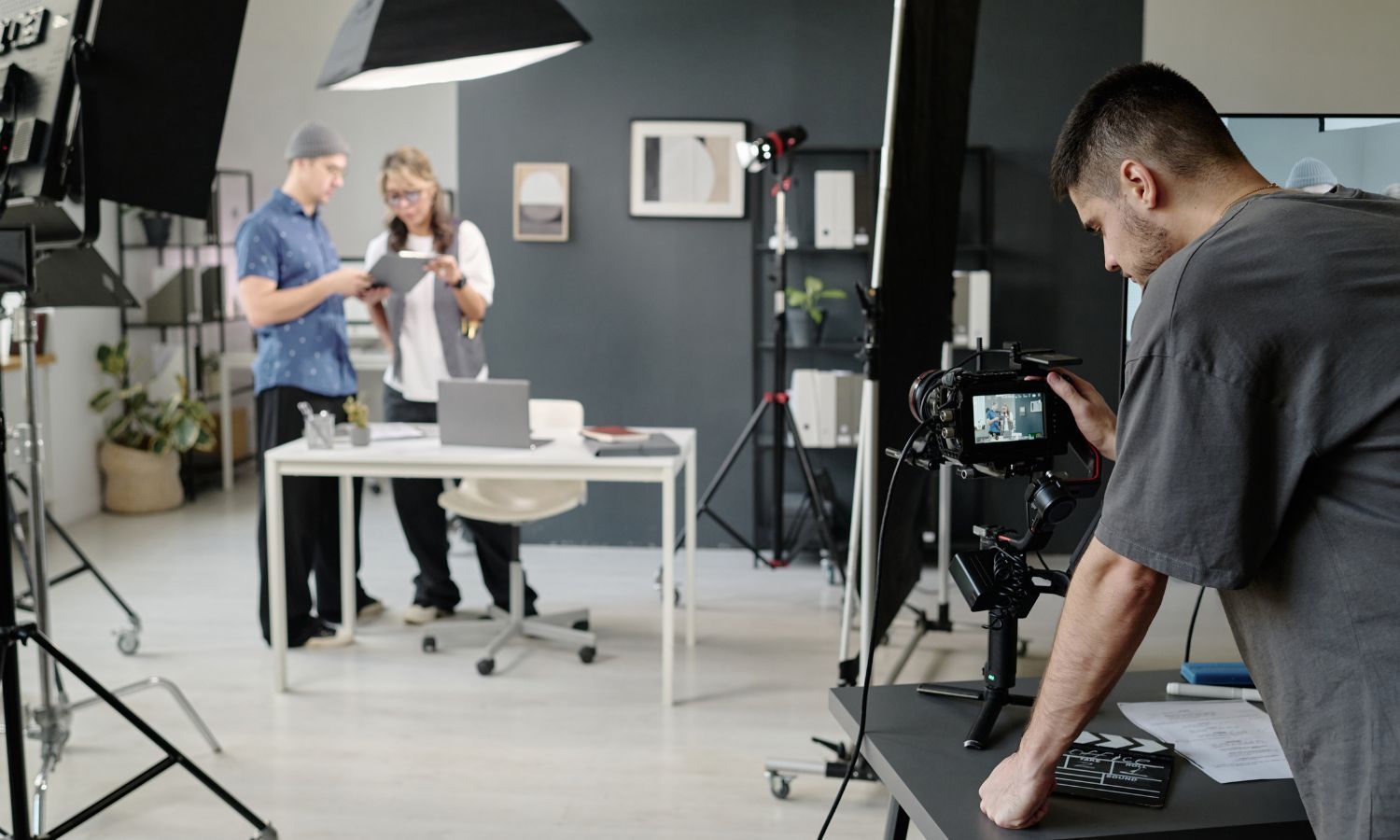 Filmmaker filming two people reviewing documents at a table in a studio.