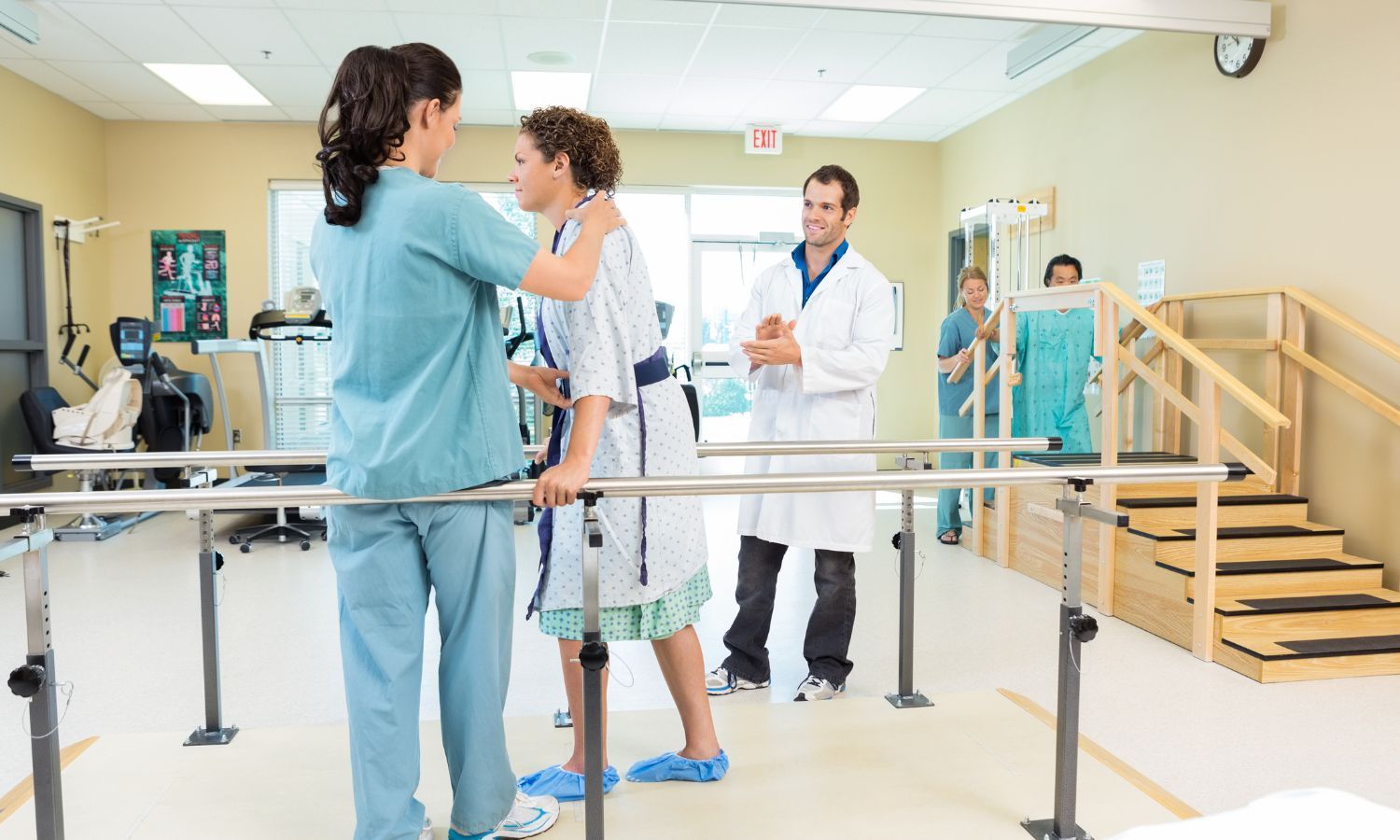 Rehabilitation patient practicing walking with support in a therapy room, guided by a nurse and observed by a doctor.