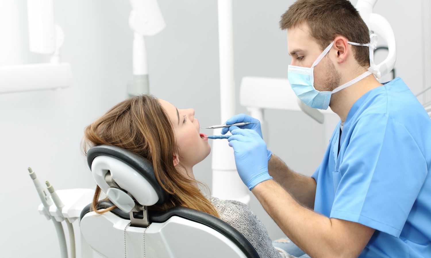 Dentist examining a patient's mouth in a dental office. Patient is seated, mouth open. Dentist in mask and gloves.