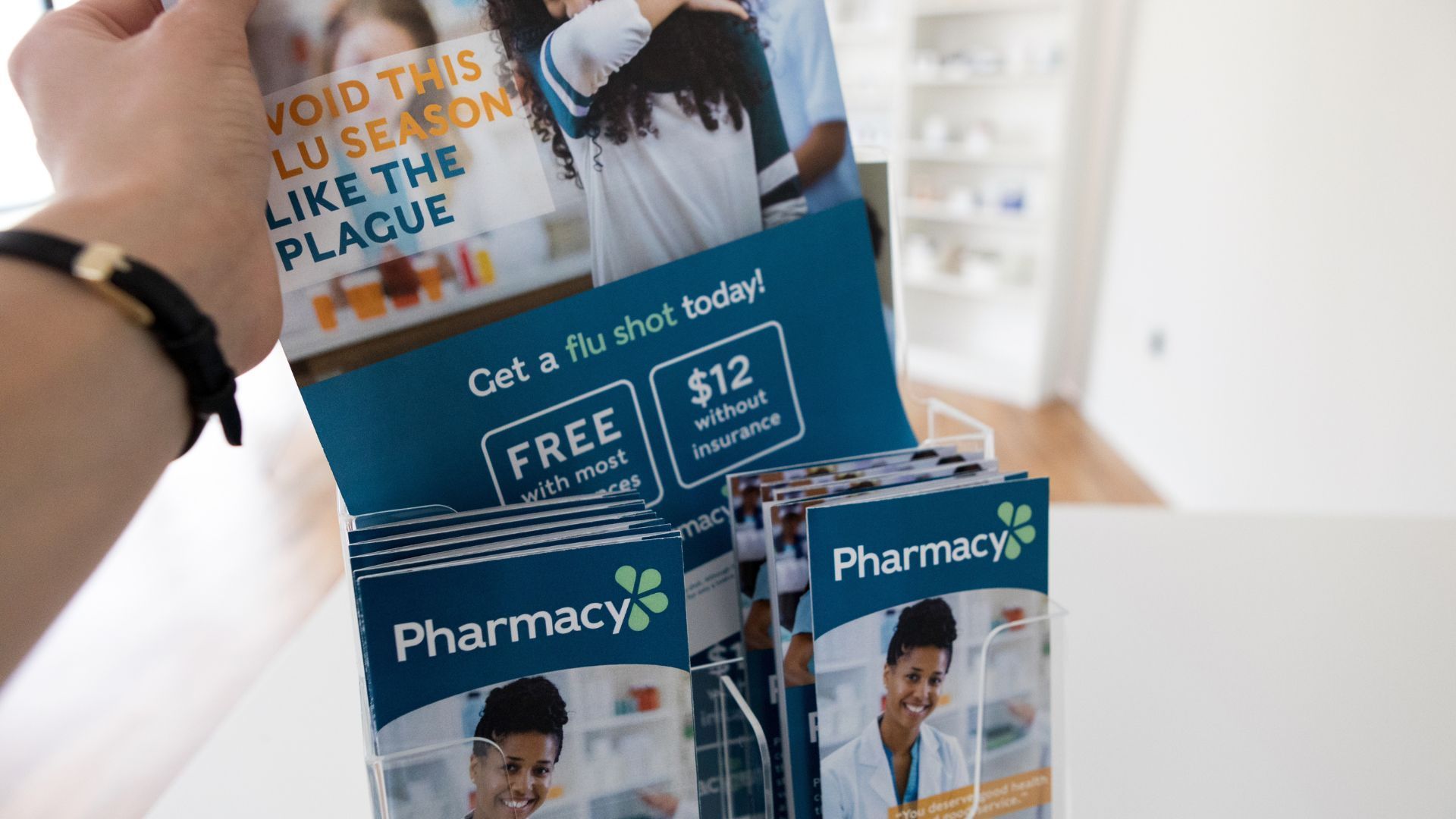 Person holding flu shot advertisement; free with insurance, $12 without. Pharmacy branding.