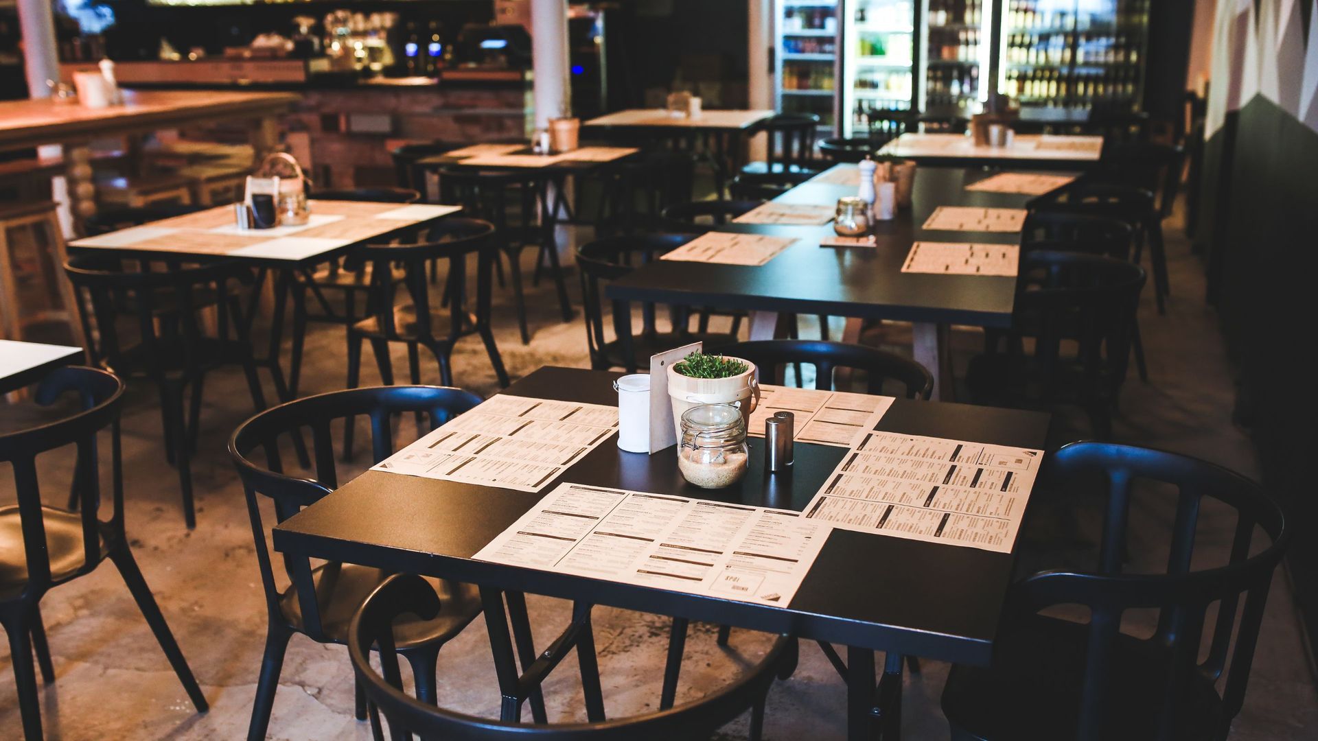 Interior of a restaurant with black tables and chairs, set for dining; a vase sits in the center of a table.