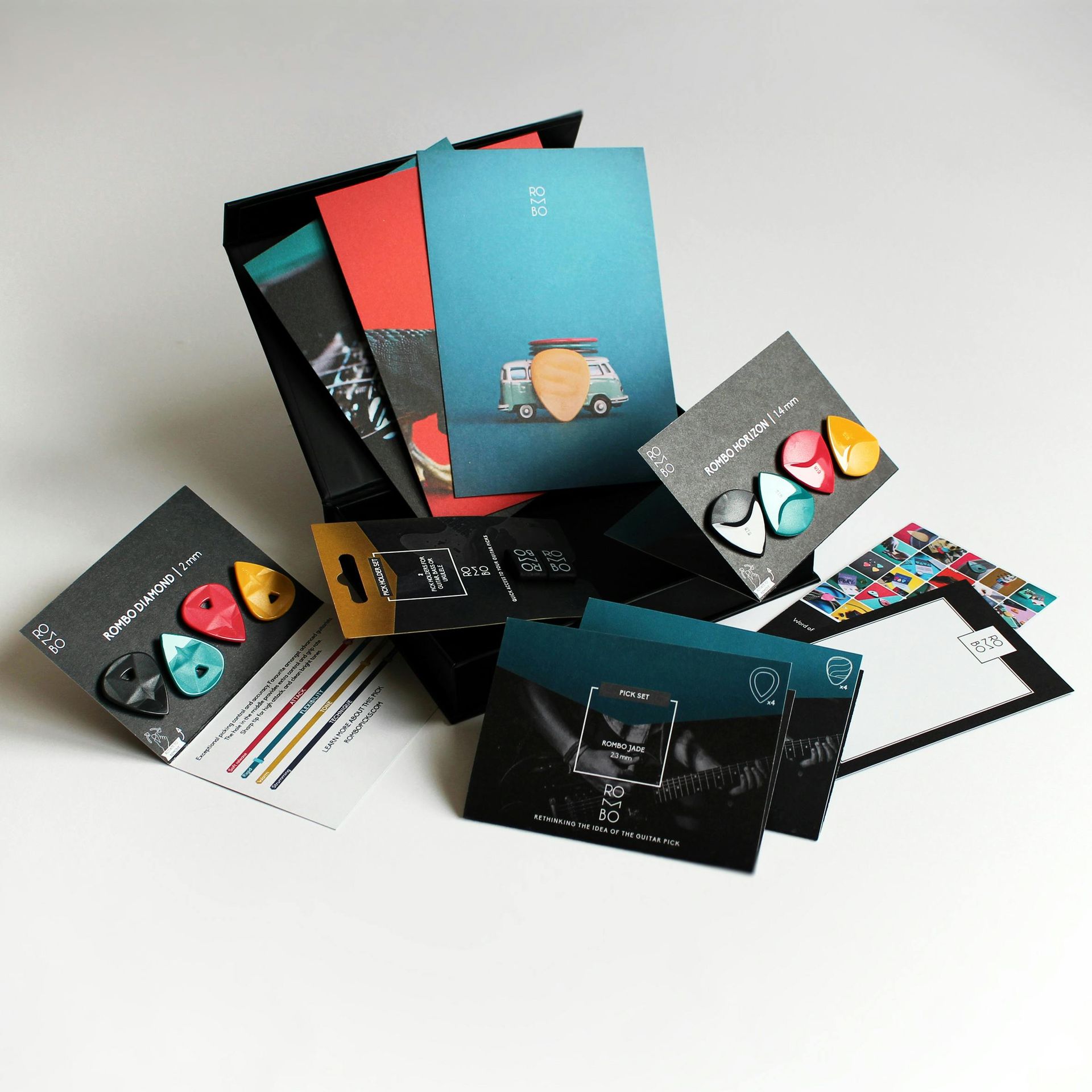 Open black box overflowing with guitar picks and cards of various colors and designs on a white surface.