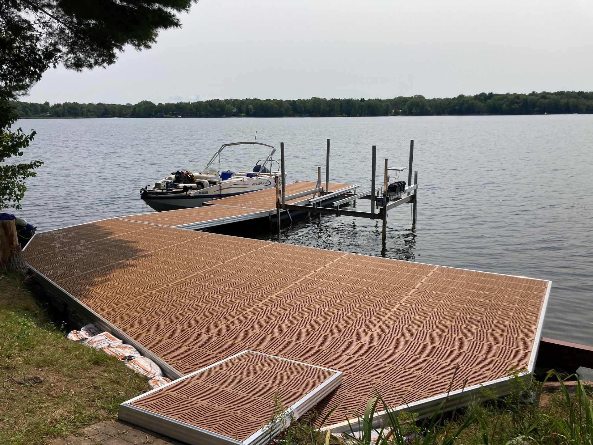 Floating dock system with boat lift extending from wooded shoreline into calm Ontario lake water
